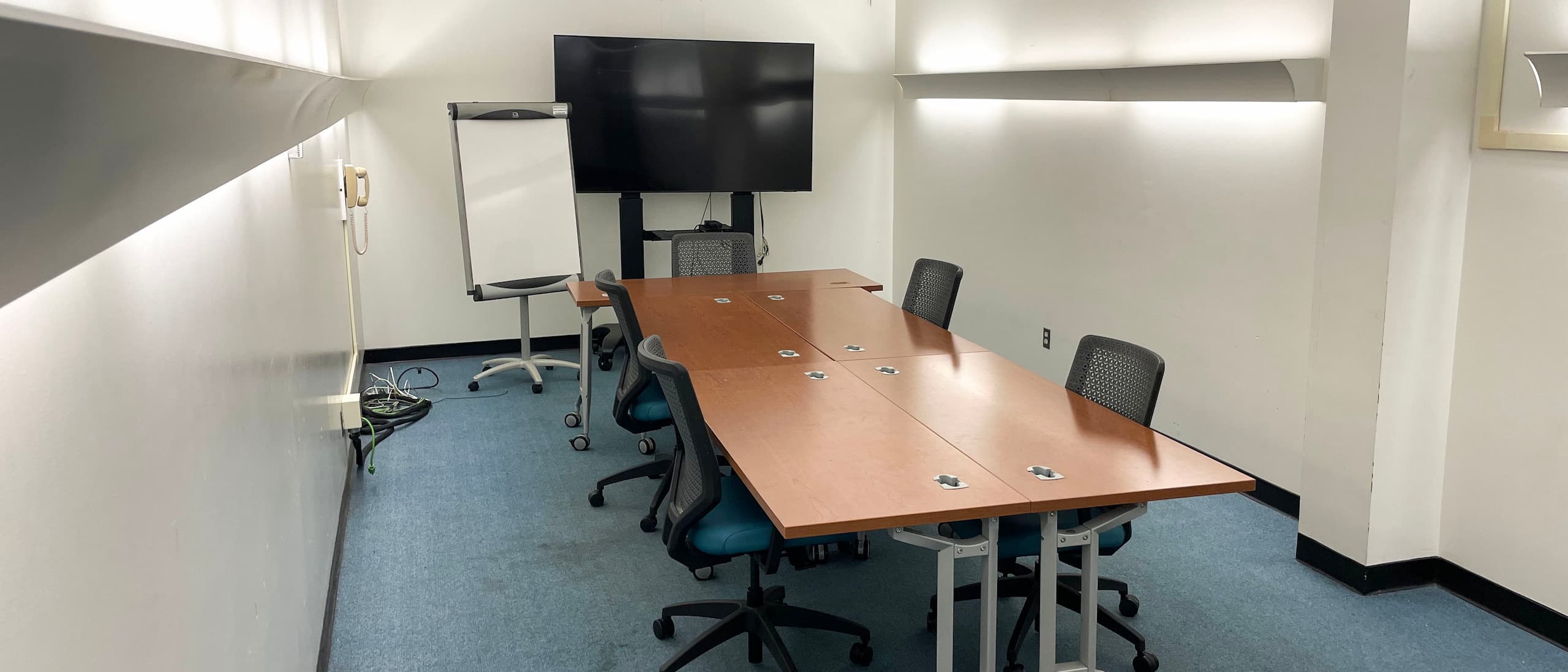 Picture of meeting room which includes table, 4 chairs, display, and whiteboard.