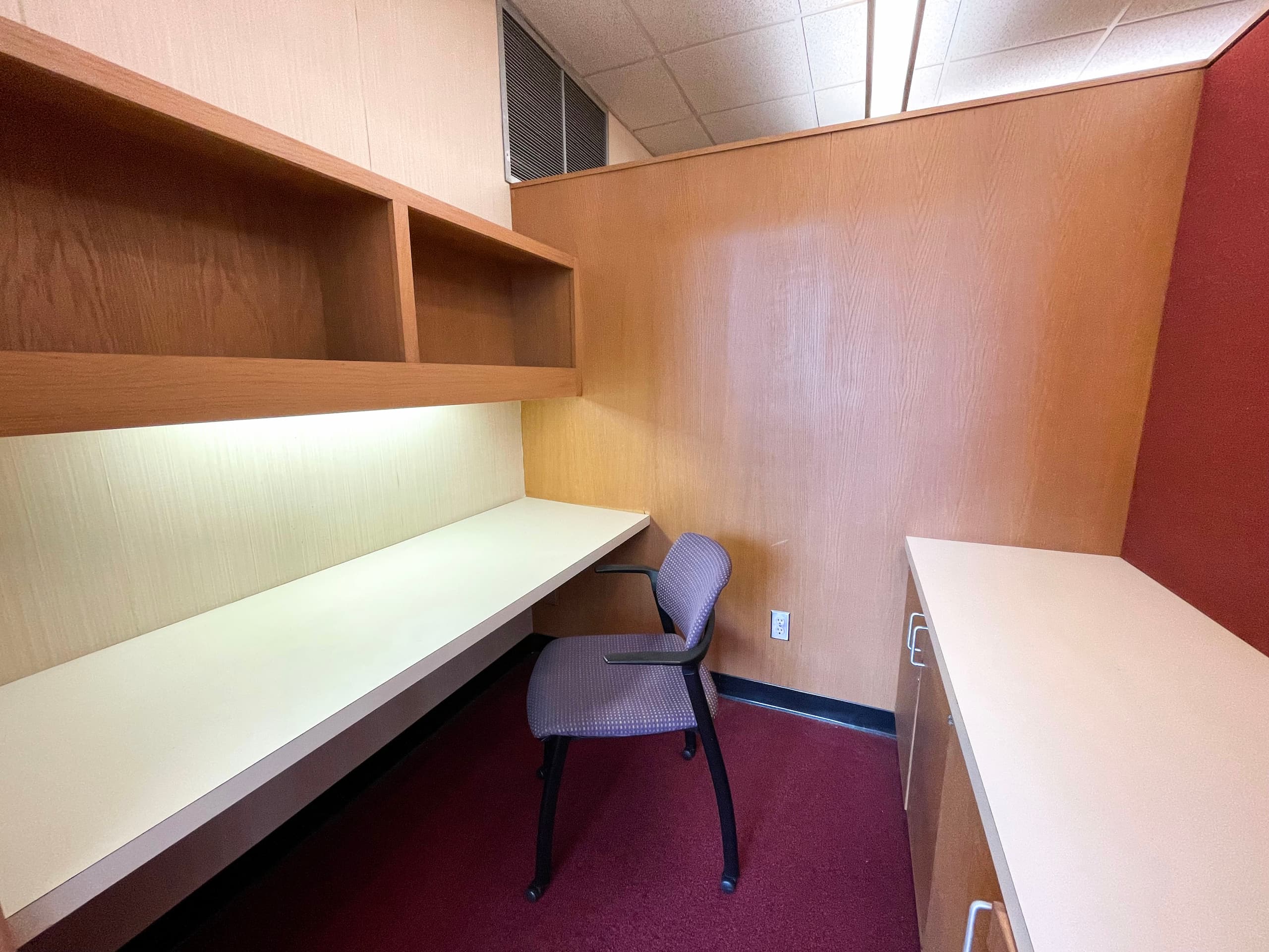 Small room with a book shelf, desk, cabinets and chair.