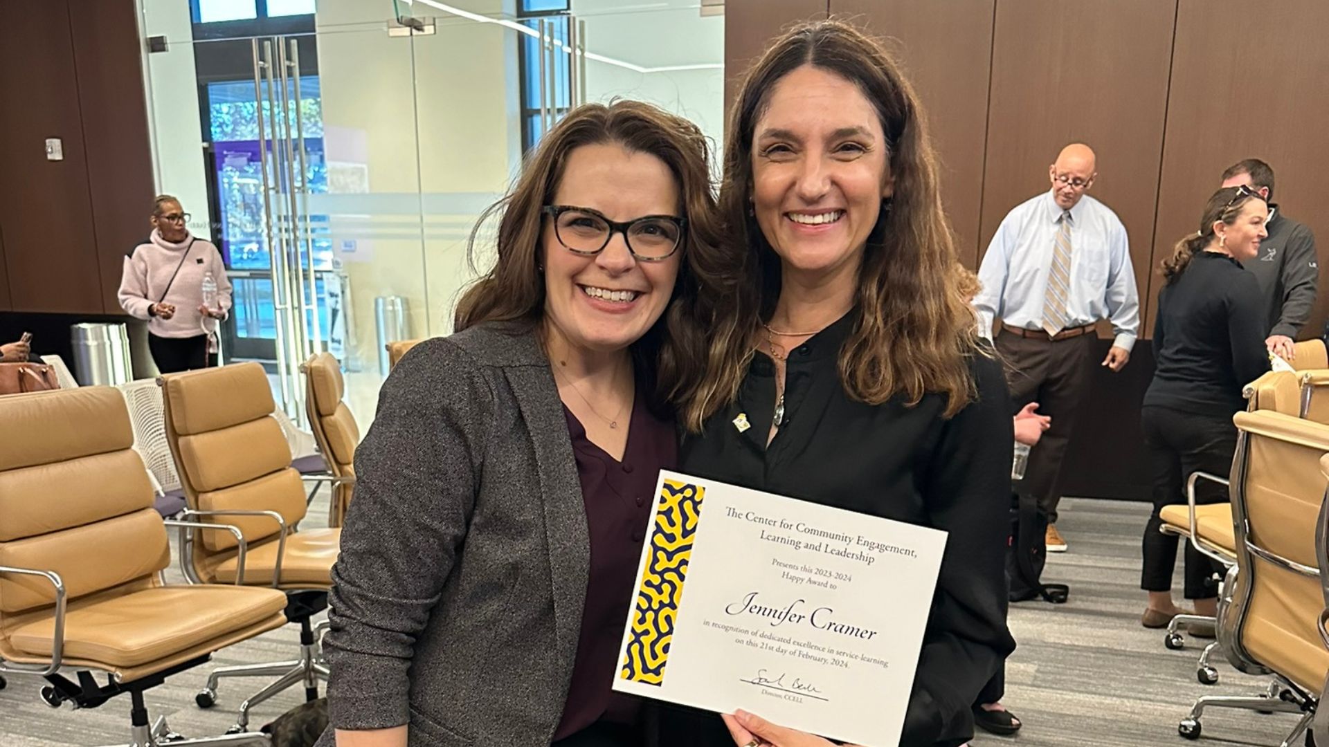 two women smile while holding a certificate