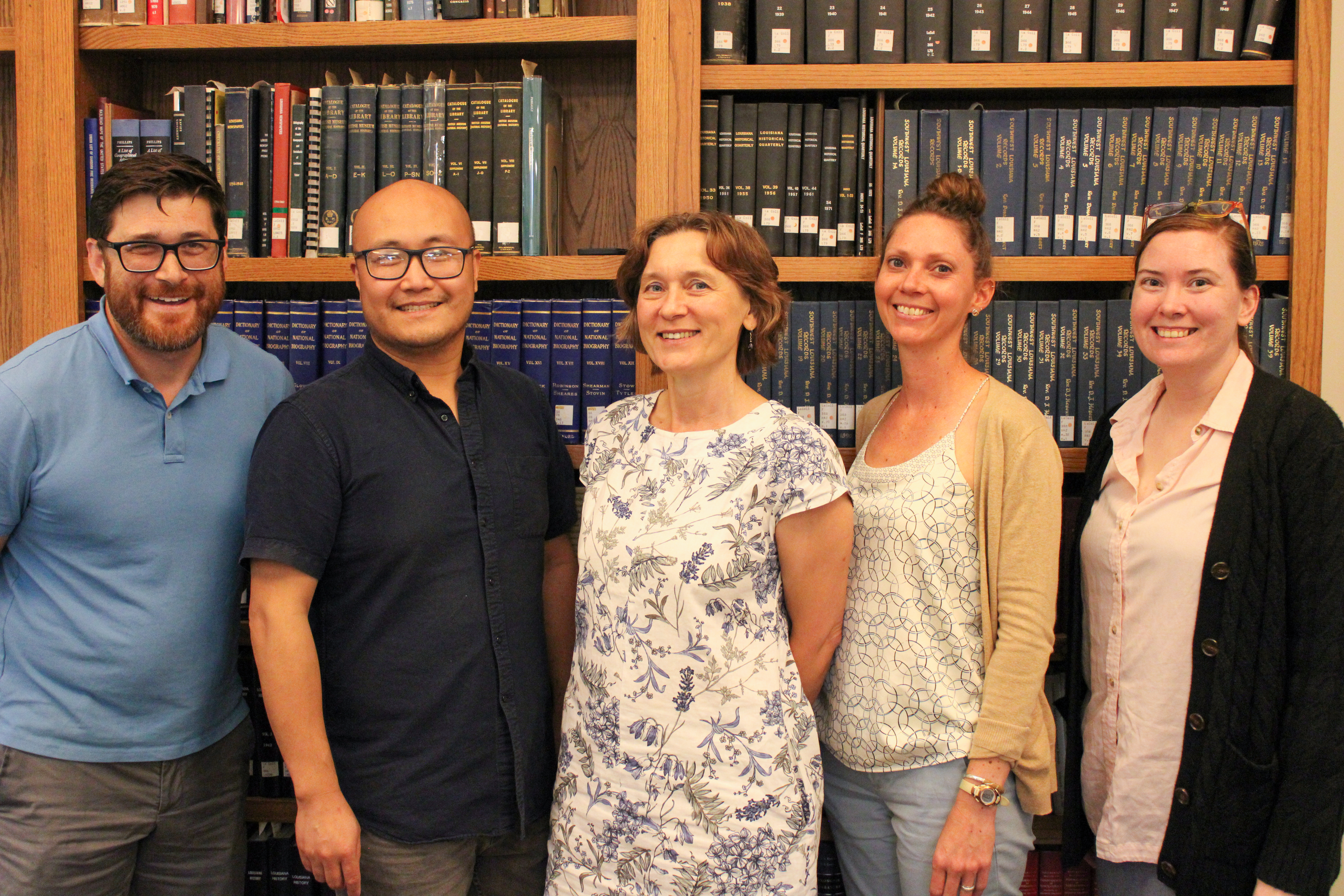 five people stand in front of a bookshelf indoors